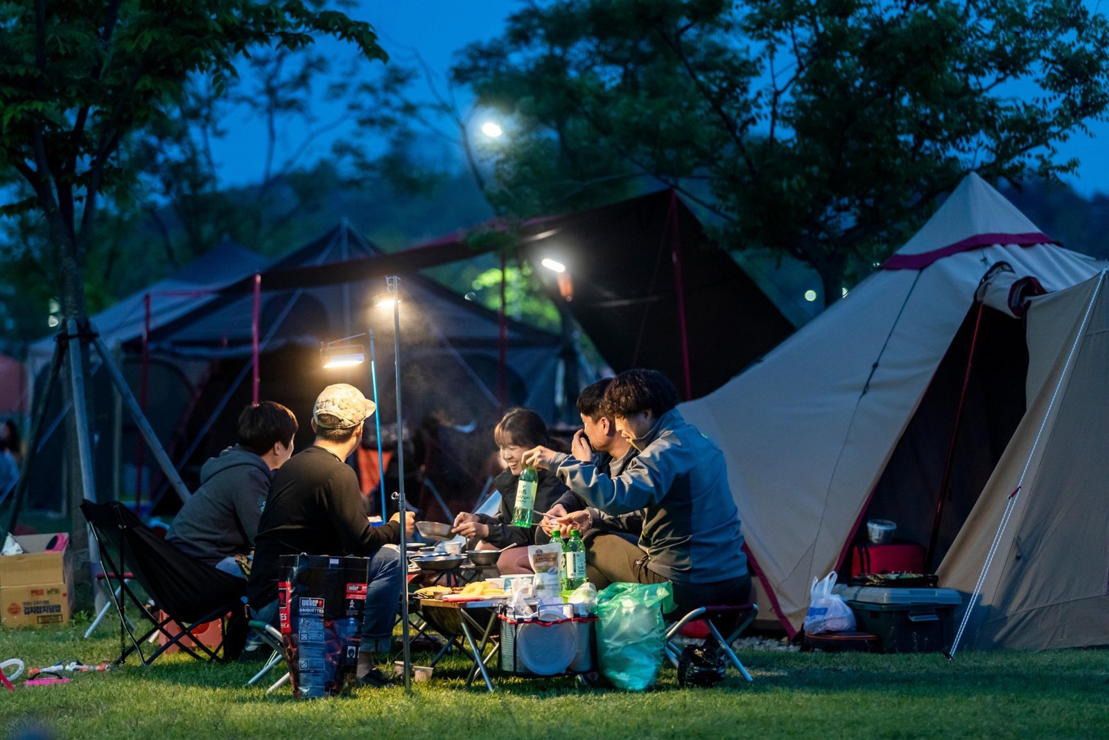 밤, 랜턴 불빛 아래 텐트 앞에서 함께 식사하는 야영 손님들